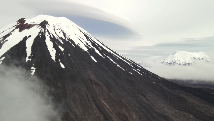 Beautiful scenery of New Zealand volcanic landscape. Mount Ngauruhoe and Mount Ruapahu, snowy peaks above clouds.