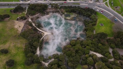 Hot steaming spring in city park, Rotorua. Aerial reveal to lakeside. Cloudy day in New Zealand