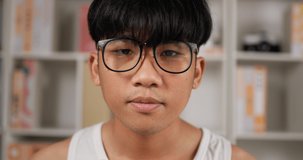 Close up face of Asian teenager man glasses smiling and looking at camera in apartment. Cute teenager student at home. Lifestyle and people concept.