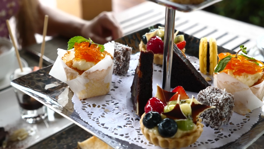 Sweet breakfast. Woman eating desserts in cafe - cakes, macaroons, tarts with berries. Female hand take a piece of pie. Traditional english afternoon tea pastries in luxury hotel. Close up