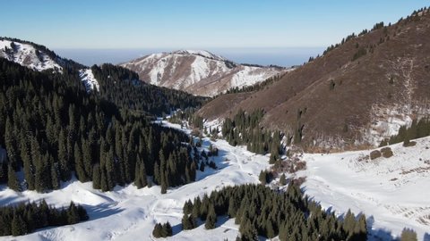 Mountains near the city of Almaty. The drone flies over the snow-covered Butakosky gorge. Sunny morning in the mountains. Fog over Almaty.