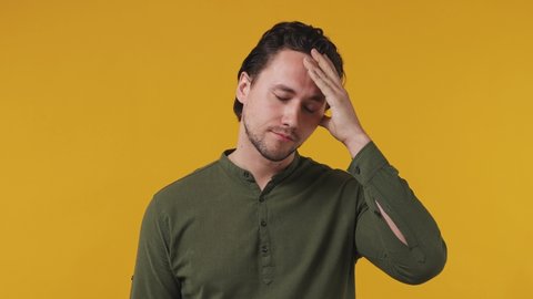 Tired sad frowning young brunet bearded man 20s wears green shirt did not get enough sleep last night after party and barely got up in the morning yawning isolated on pastel plain yellow background