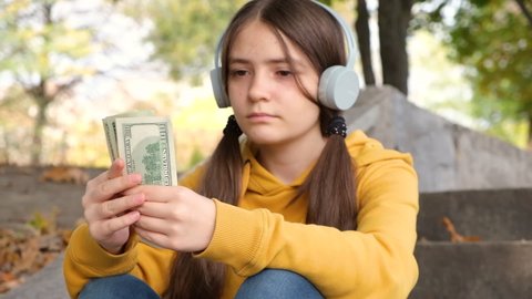 A teenage girl in headphones counts dollar bills, pocket money