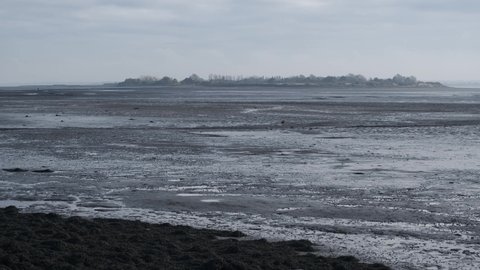 Distant view of mysterious Osea Island private retreat across mud flats. Low tide on river Blackwater estuary. Overcast winter day outdoors. United Kingdom, Essex, Maldon, November 11, 2021
