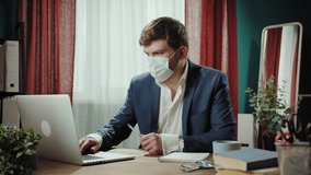Executive senior CEO businessman in medical mask working online on laptop, remote office, man typing. Financial director writing notes, closing computer, home office. 