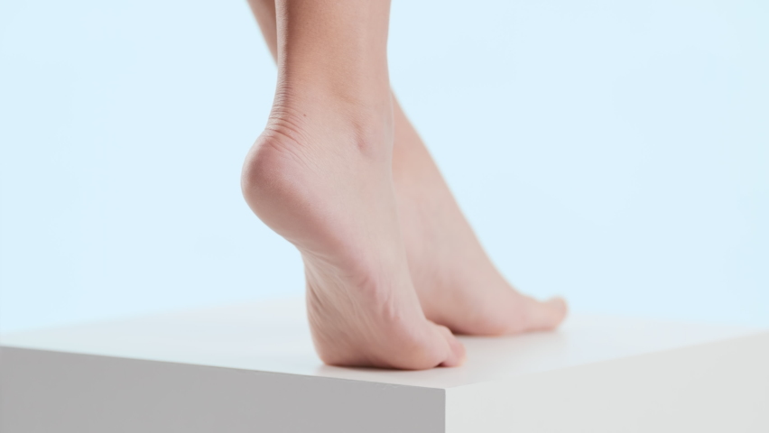 Horizontal close-up shot of woman touches her tiptoe foot on the white cube platform on pale blue background | Anti cracked foot concept Royalty-Free Stock Footage #1082254469