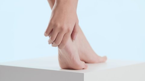 Horizontal close-up shot of woman touches her tiptoe foot on the white cube platform on pale blue background | Anti cracked foot concept