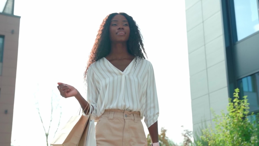 Happy young black African woman customer shopper walking on city street holding shopping bags using cell phone mobile app buying fashion sale clothes online in ecommerce digital store on smartphone. Royalty-Free Stock Footage #1082255429