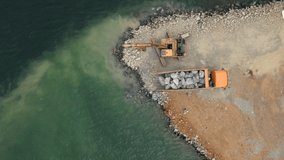 Aerial video. View from abobe and excavator working on building a land in a sea. Filling the shore with a stone. Coastline Strengthening, Erosion Control,Fighting the ocean Level Rise. Coastal