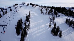 Panoramic top view from drone on cable way in ski resort. Ski lift elevator transporting skiers and snowboarders on snowy winter slope at mountain resort, many people. UHD 4k video