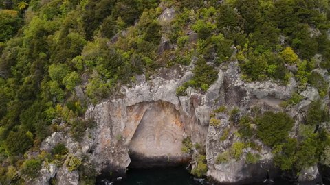 Maori mask carving, artwork in New Zealand. Spectacular sculpture carved to rocky cliff, Lake Taupo - Aerial tilt down