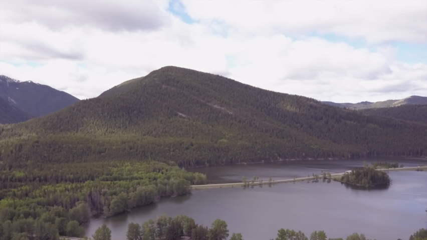 Highway traffic drives on road built across small blue mountain lake
