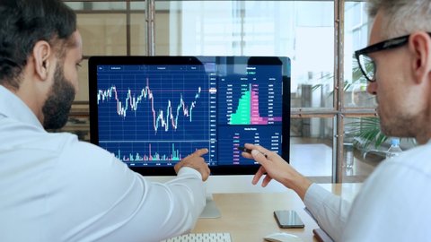 Two traders brokers stock exchange market investors discussing crypto trading charts growth using pc computer pointing at screen analyzing financial risks, investment profit forecast. Over shoulder: film stockowy
