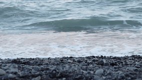 Sea surf on a pebble beach. Waves ride pebbles on the coastline. Selective focus video. Natural background.