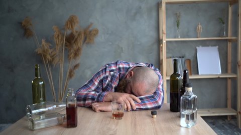 Depressed drunk man holding a drink and sleeping at home at the table. the concept of depression and alcoholism in the muschin.