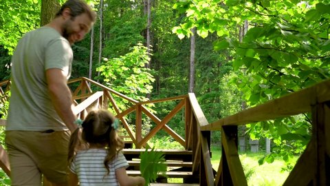 Dad put his daughter on his shoulders and tells stories about animals. Family vacation in the woods. Father's day concept. Family travel with children. Hiking trail with wooden deck in a forest.