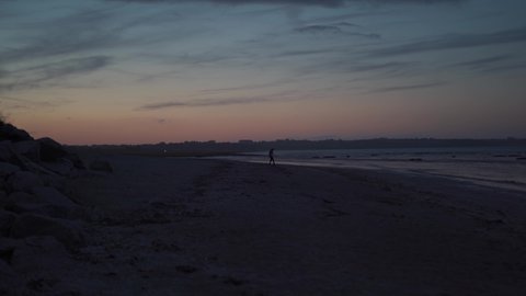 Ocean ebb theme in northern france in brittany region. Man tourist walks along shore at sunset. Atlantic coast. Atlantic Ocean beach during low tide, with sand dunes. Atmospheric and calming sunset