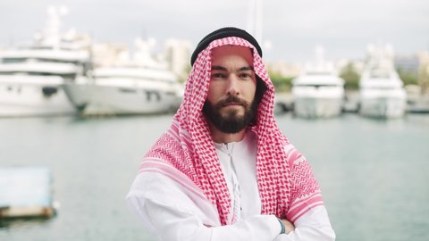 Young serious confident saudi businessman in traditional wear posing with arms crossed in port