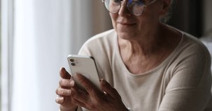 Older adult people and tech. Close up of modern mobile phone gadget used by aged female retiree at home. Confident mature woman wear glasses look on smartphone screen work in convenient web app online