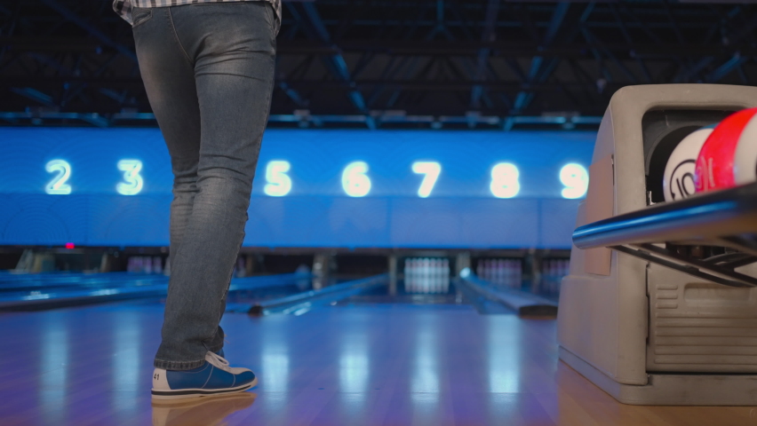 The camera follows one Caucasian man throwing a bowling ball on the playing track and jumping rejoicing in the downed pins. One man bowling in slow motion