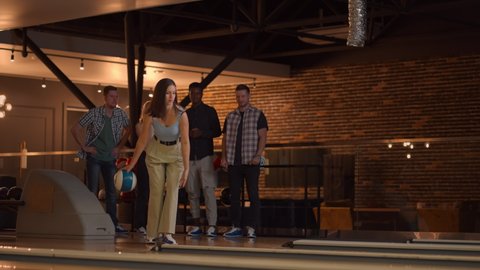 A Caucasian brunette woman throws a bowling ball and knocks out a shot with one throw and hugs and rejoices with her friends. Multi-ethnic group of friends bowling