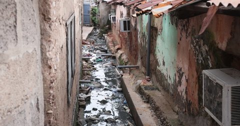 NIMA, GHANA - 23 OCT 2021: Alley between homes raw sewer ditch Accra Ghana. Market residential area. Pollution and garbage. Homes low income poverty of Africa.