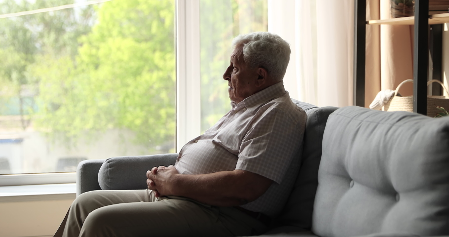 Sad unhappy mature male retiree sit on couch alone look at window with spring view feel abandoned depressed suffer of weakness ageing retirement problems. Upset elderly man grieving about passed youth Royalty-Free Stock Footage #1082286253