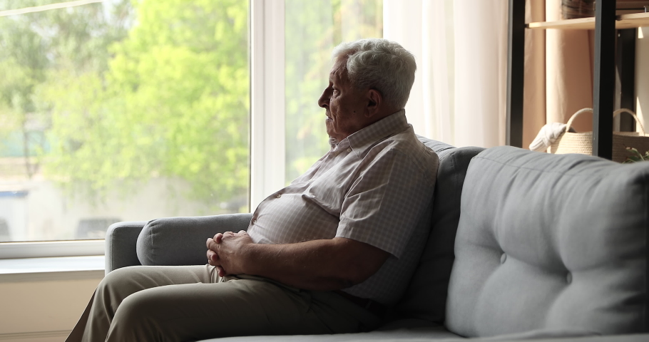 Sad unhappy mature male retiree sit on couch alone look at window with spring view feel abandoned depressed suffer of weakness ageing retirement problems. Upset elderly man grieving about passed youth Royalty-Free Stock Footage #1082286253