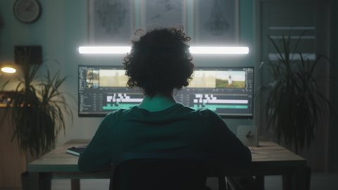 Zoom in view of anonymous man watching and editing farm video on computer while working on remote project at night at home