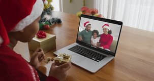 African american woman with santa hat using laptop for christmas video call with family on screen. christmas, festivity and communication technology.