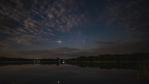 Timelapse of the movement of the Milky Way over the lake in summer. Timelapse of the movement of the starry sky with clouds over the lake on a summer night in Russia