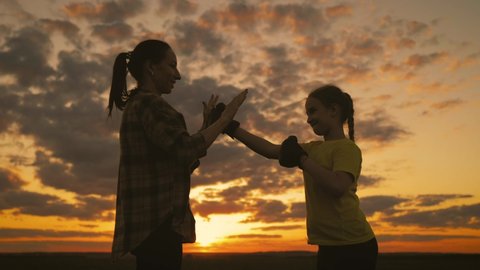 Active daughter training boxing with her young mother. Girl boxer goes in for sports on the background of sunset in the field. A family silhouette boxing together while on sunset.