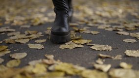 woman is walking in park in autumn, closeup of feet, black boots are stepping on asphalt