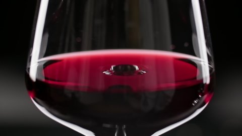 Wineglass with slowly falling drops. Close-up of wine drop falling into red wine. Slow motion of pouring red wine into goblet.