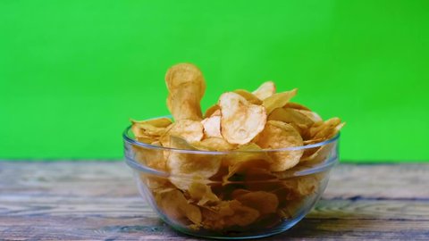 Glass cup with potato chips on a wooden table with a chroma key background. Different hands take potato chips from the cup against the background of the chromakey.