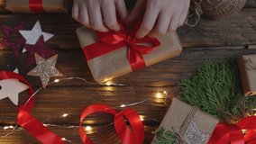 female woman hands wrapping Christmas presents gift box with brown craft paper, tying red ribbon bow on wooden desk with new year ornaments: stars light garland and green coniferous. top view DIY home - Powered by Shutterstock - Get 15% off with code: PIKWIZARD15