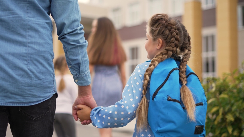 Happy family. Father and daughter go to school. Schoolgirl with backpack holds her father hand. Family goes to school. Male hand helping child. Father and daughter schoolgirl are walk in school park | Shutterstock HD Video #1082300551