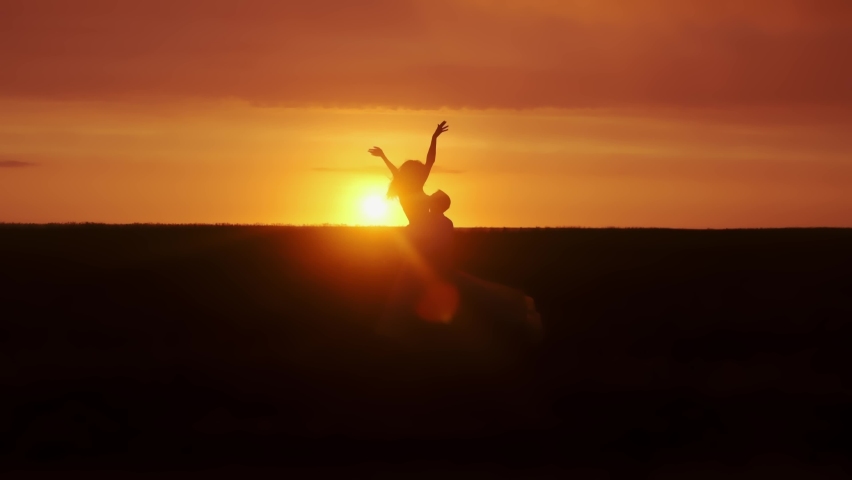 Silhouette of man and woman at sunset. Beautiful girl kisses guy in a deserted field, leaves and rises to hold her hands in slow motion. A romantic date and love on nature of loving happy couple