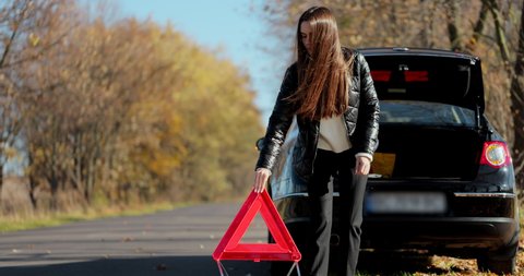 Sad disappointed woman on broken car. Woman driver installing red triangle sign. Broken car accident. Woman driver places emergency stop sign.