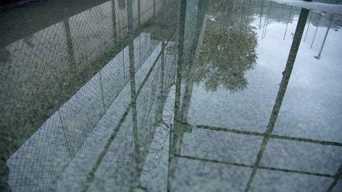 Prison chain link fence or rabitz with barbed wire with cloudy sky reflects in the pond