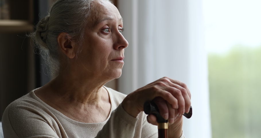 Cropped close up of depressed hoary older adult female living with physical disability sit by window alone hold stick. Retired old woman with walking difficulties look at distance feel weak hopeless | Shutterstock HD Video #1082309506