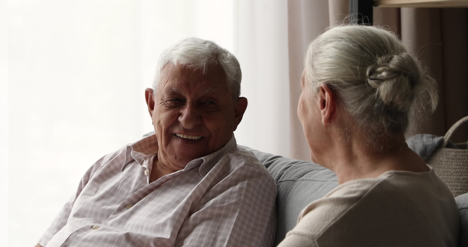 Positive older age male female on pension spouses neighbors friends chat on comfy couch engaged in pleasant dialogue relax at home together. Elderly couple talk discuss interesting topics having fun Royalty-Free Stock Footage #1082309569