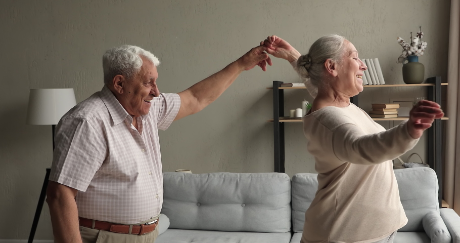 Affectionate middle aged couple grandparents dance waltz at living room together having date at home. Romantic mature husband hold hand of beloved smiling old lady wife move in beautiful music rhythm Royalty-Free Stock Footage #1082309626