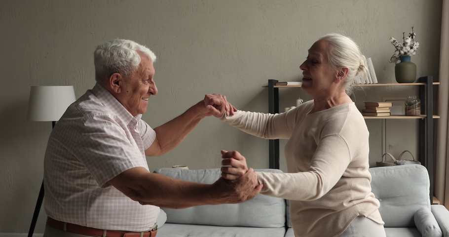 Affectionate middle aged couple grandparents dance waltz at living room together having date at home. Romantic mature husband hold hand of beloved smiling old lady wife move in beautiful music rhythm Royalty-Free Stock Footage #1082309626