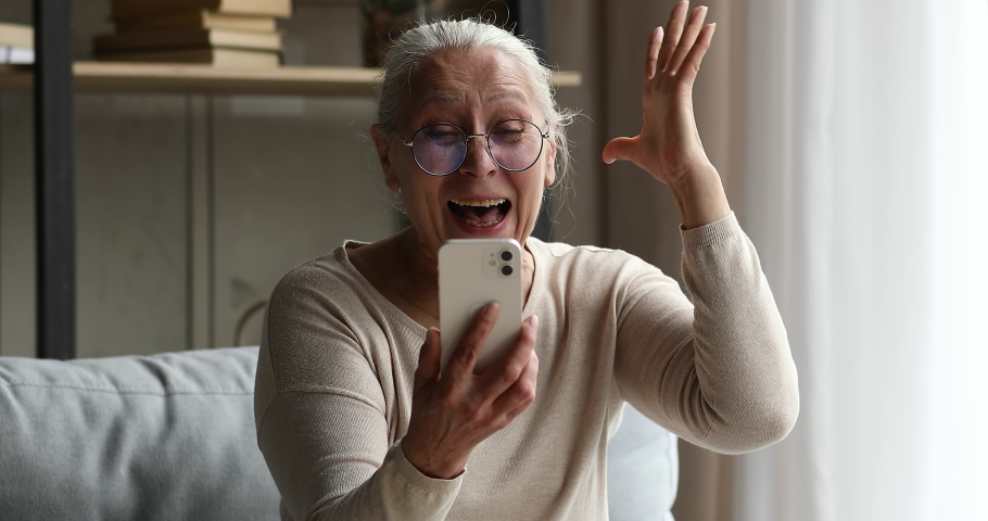 Excited joyful old age female discovered virtual activity world on retirement amazed with winning online interactive game on smartphone. Active mature lady pensioner get prize reward in web lottery Royalty-Free Stock Footage #1082309644