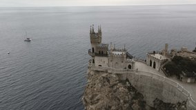 Departure of the drone from Swallow's nest in Crimea 4k video. The castle tower is on the edge of a high cliff. White yacht on the background of the Black Sea