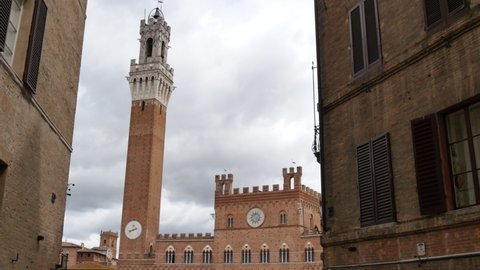 Siena, Tuscany, Italy JULY, 15, 2016 Torre del Mangia is a tower in Piazza del Campo Siena's main square with a crowd of tourists, Vide angle tilt view surrounded by historic buildings