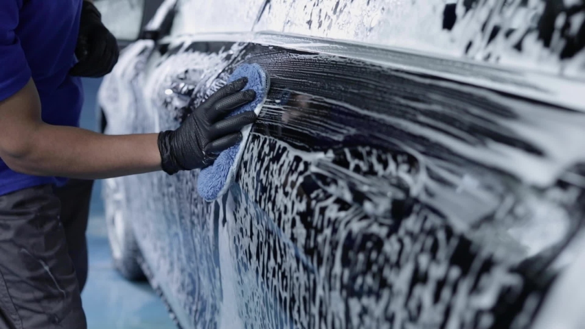 Closer look of a man while professionally cleaning the outside of the car with a sponge and detergent making slow and gently moves. 