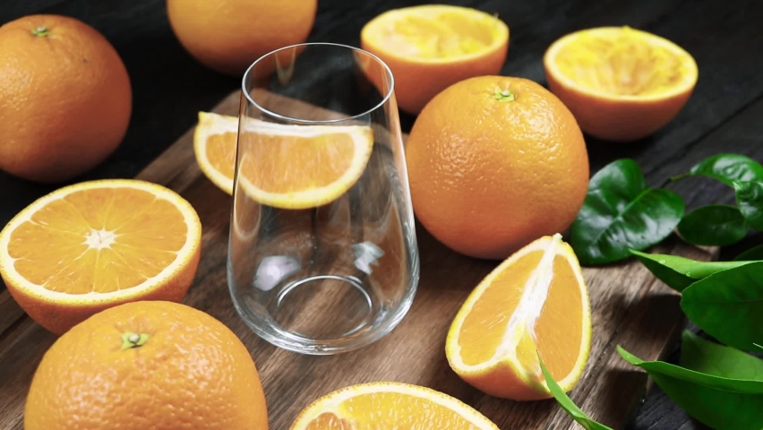 Fresh orange juice is poured into a  glass. Fresh Orange fruits with green leaves on a wooden background. Healthy vegan food. Vitamins food.Ripe oranges.  Royalty-Free Stock Footage #1082323681
