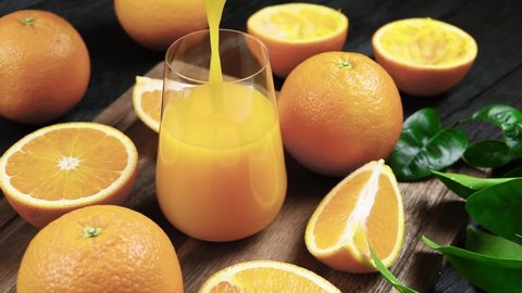 Fresh orange juice is poured into a  glass. Fresh Orange fruits with green leaves on a wooden background. Healthy vegan food. Vitamins food.Ripe oranges. 